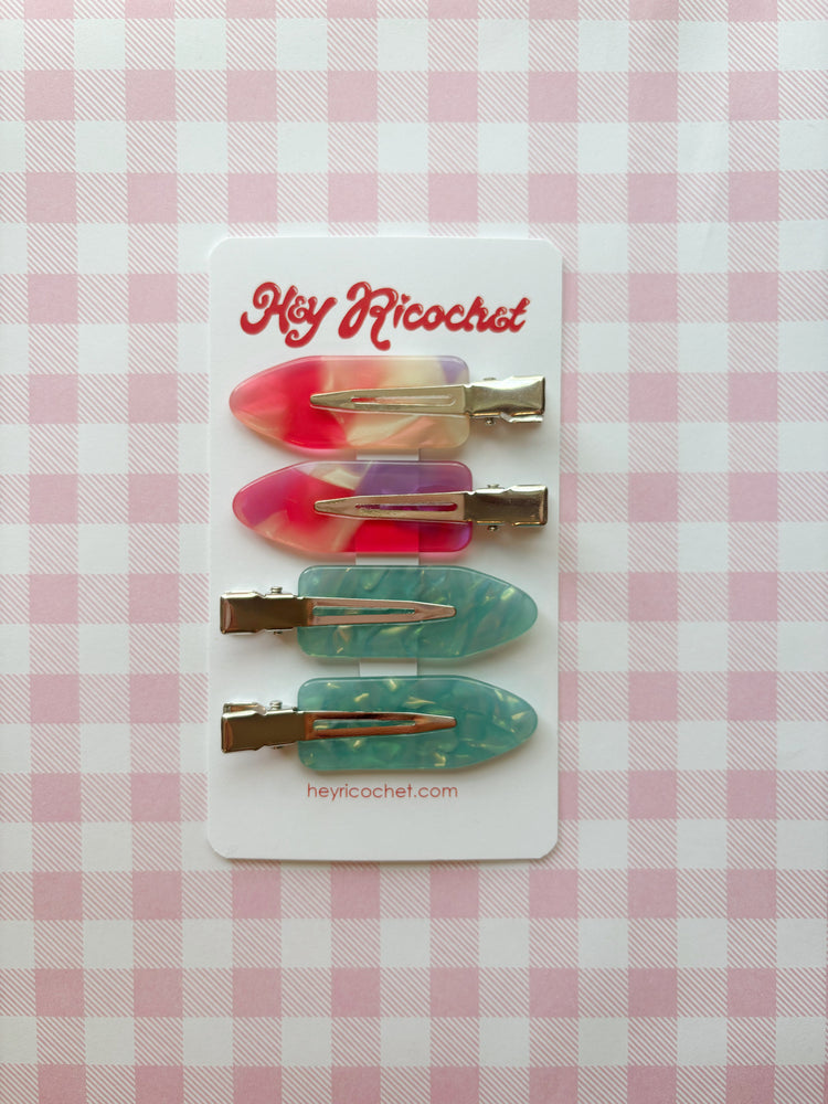 Set of colorful hair clips on a card with 'Hey Ricochet' branding against a pink checkered background.