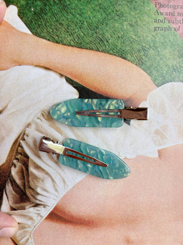 Two green hair clips on a person's arm with a magazine in the background