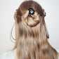 Long light brown hair styled in a half-up bun with a small black hair accessory, shown from the back on a model against a plain light background.