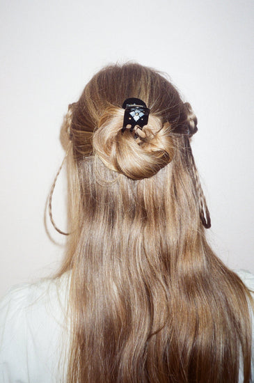 Long light brown hair styled in a half-up bun with a small black hair accessory, shown from the back on a model against a plain light background.