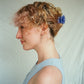 Woman with styled hair and a blue hair clip against a plain background