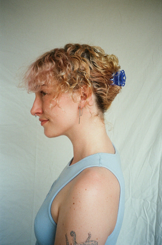 Woman with styled hair and a blue hair clip against a plain background
