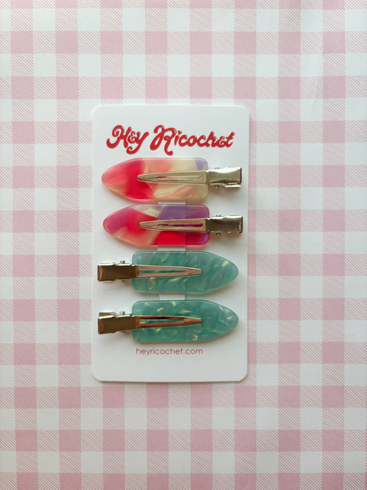 Set of colorful hair clips on a card with 'Hey Ricochet' branding against a pink checkered background.