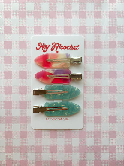 Set of colorful hair clips on a card with 'Hey Ricochet' branding against a pink checkered background.